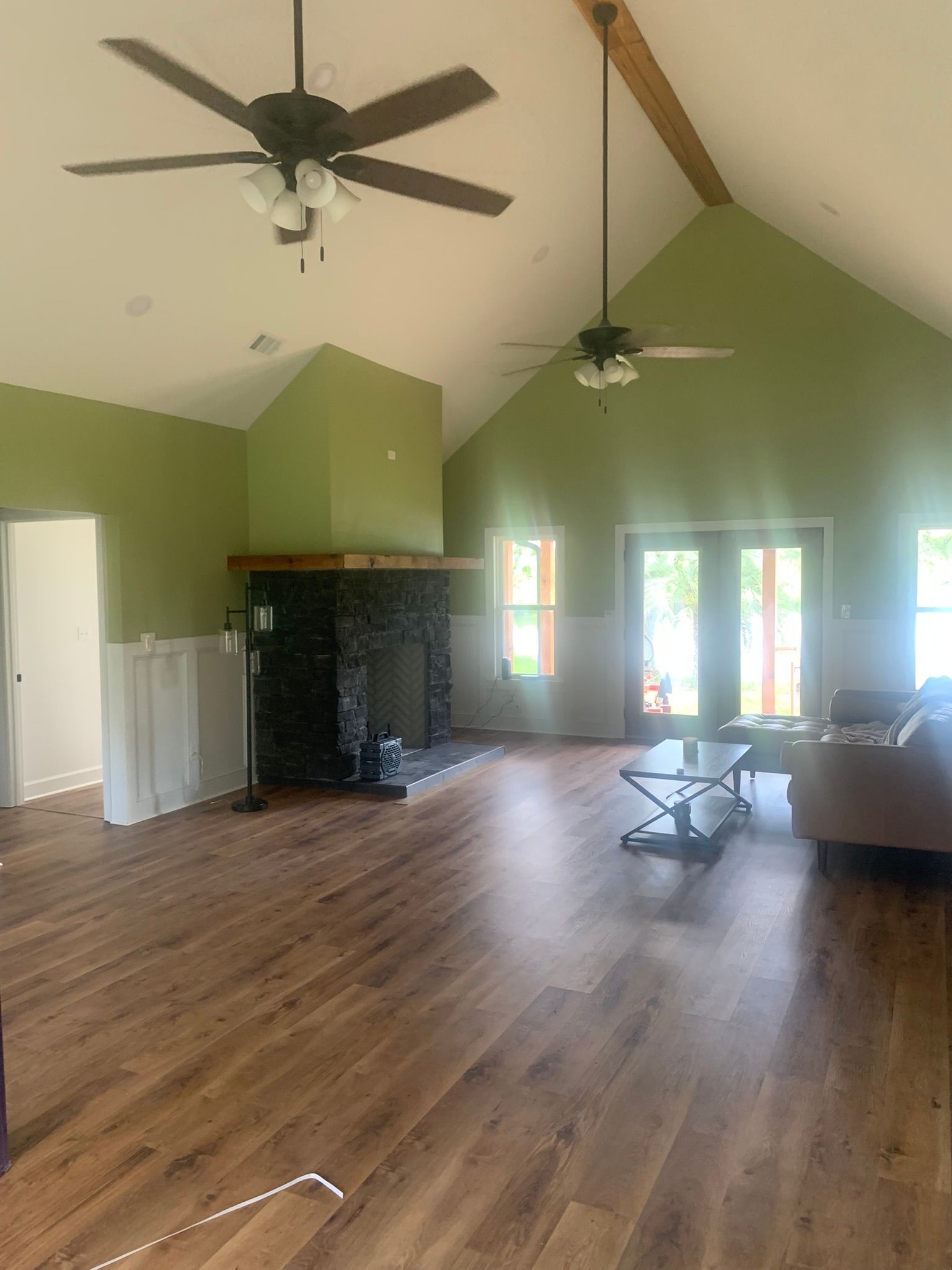 A large, green-walled living room with wood-look flooring, a fireplace, and two ceiling fans.