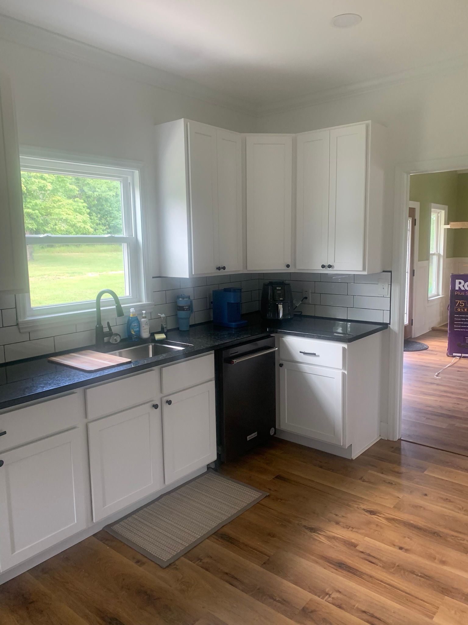 White kitchen with black countertops, stainless steel appliances, and hardwood floors.