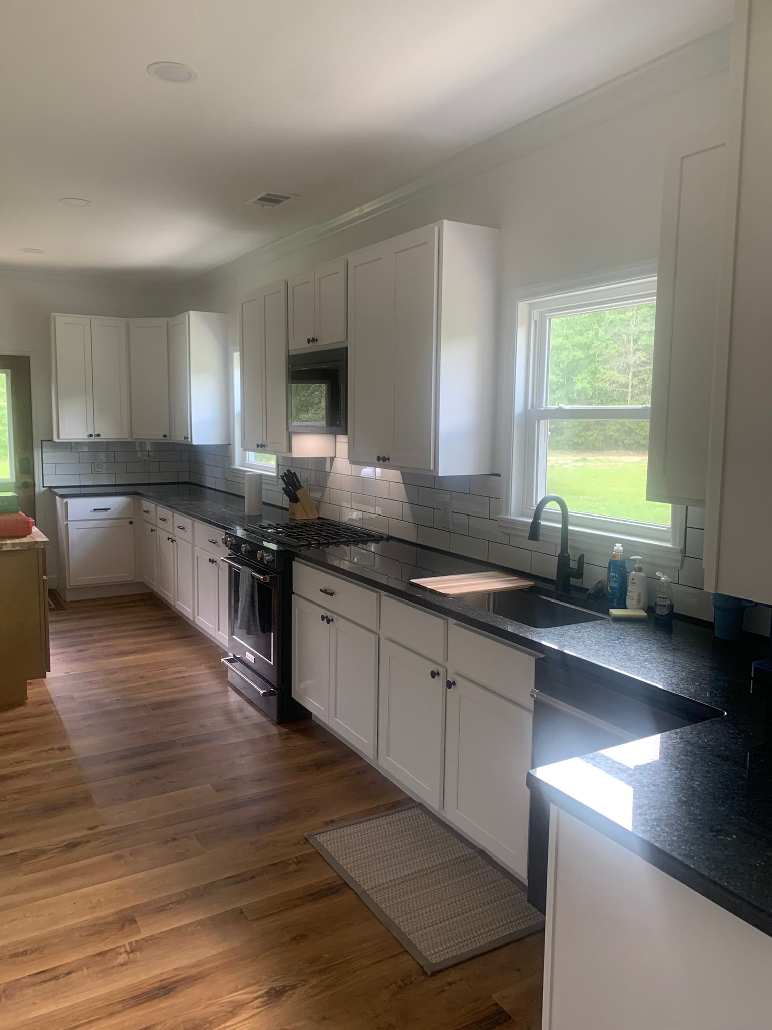White kitchen with black countertops, cabinets, and appliances. Dark wood floor.
