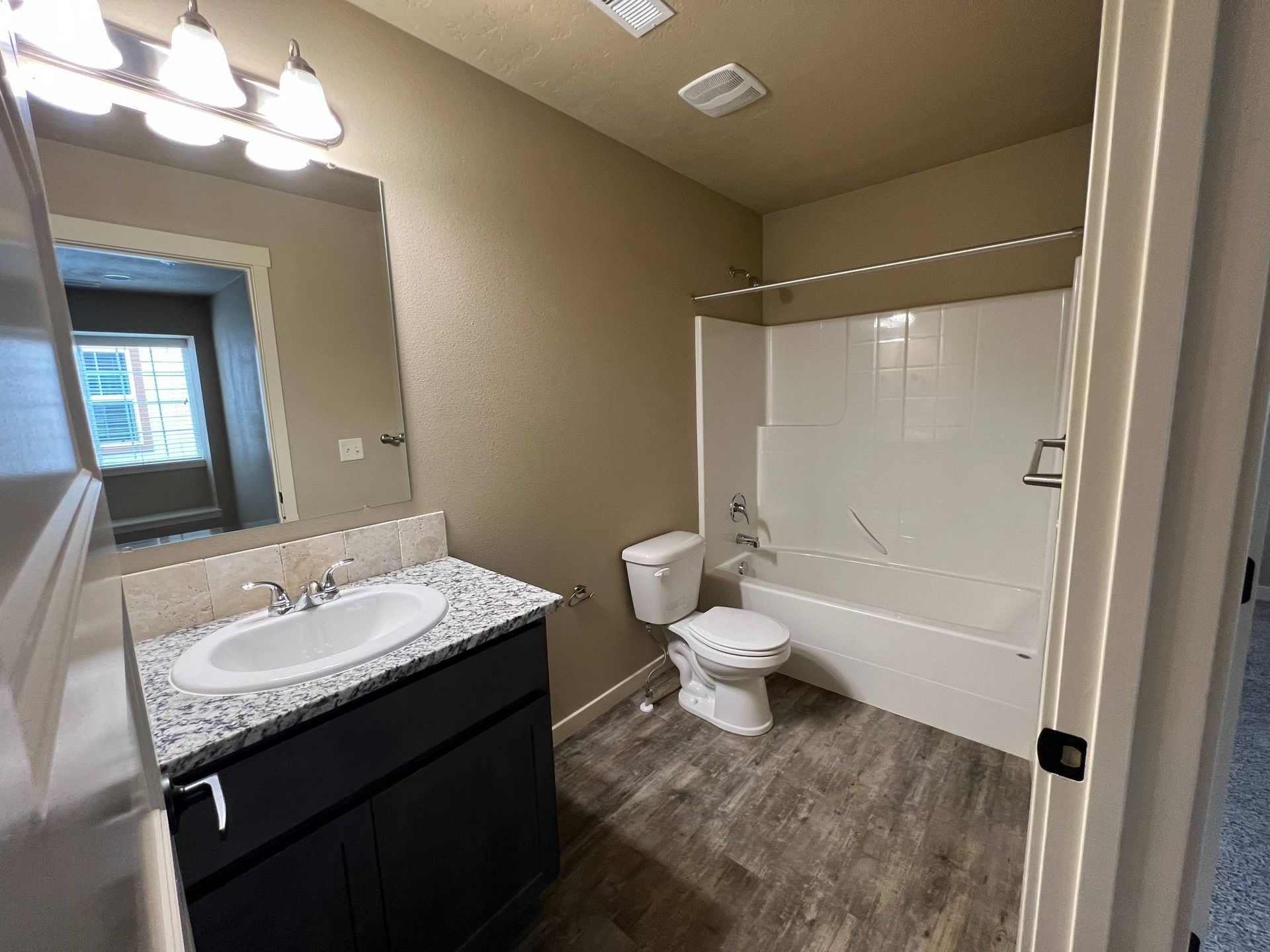 Bathroom with vanity, toilet, and bathtub. Gray countertop and flooring. Beige walls.