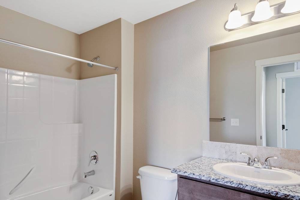 Bathroom with white tub, toilet, vanity, and tan walls.