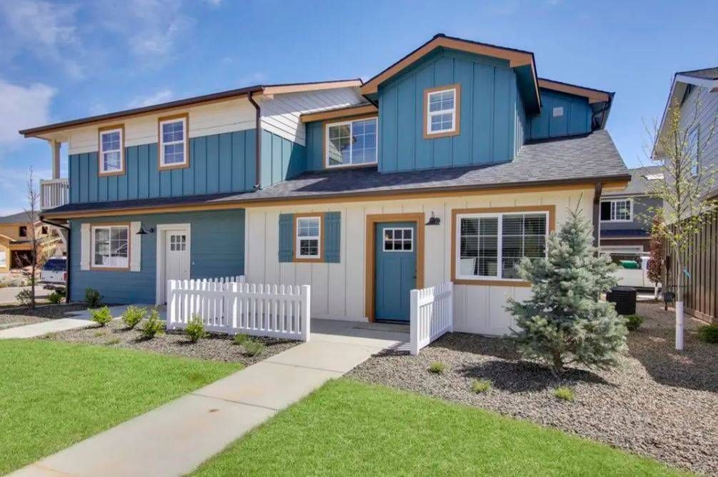 Pool area with lounge chairs, a building with a covered patio, and houses under a clear blue sky.