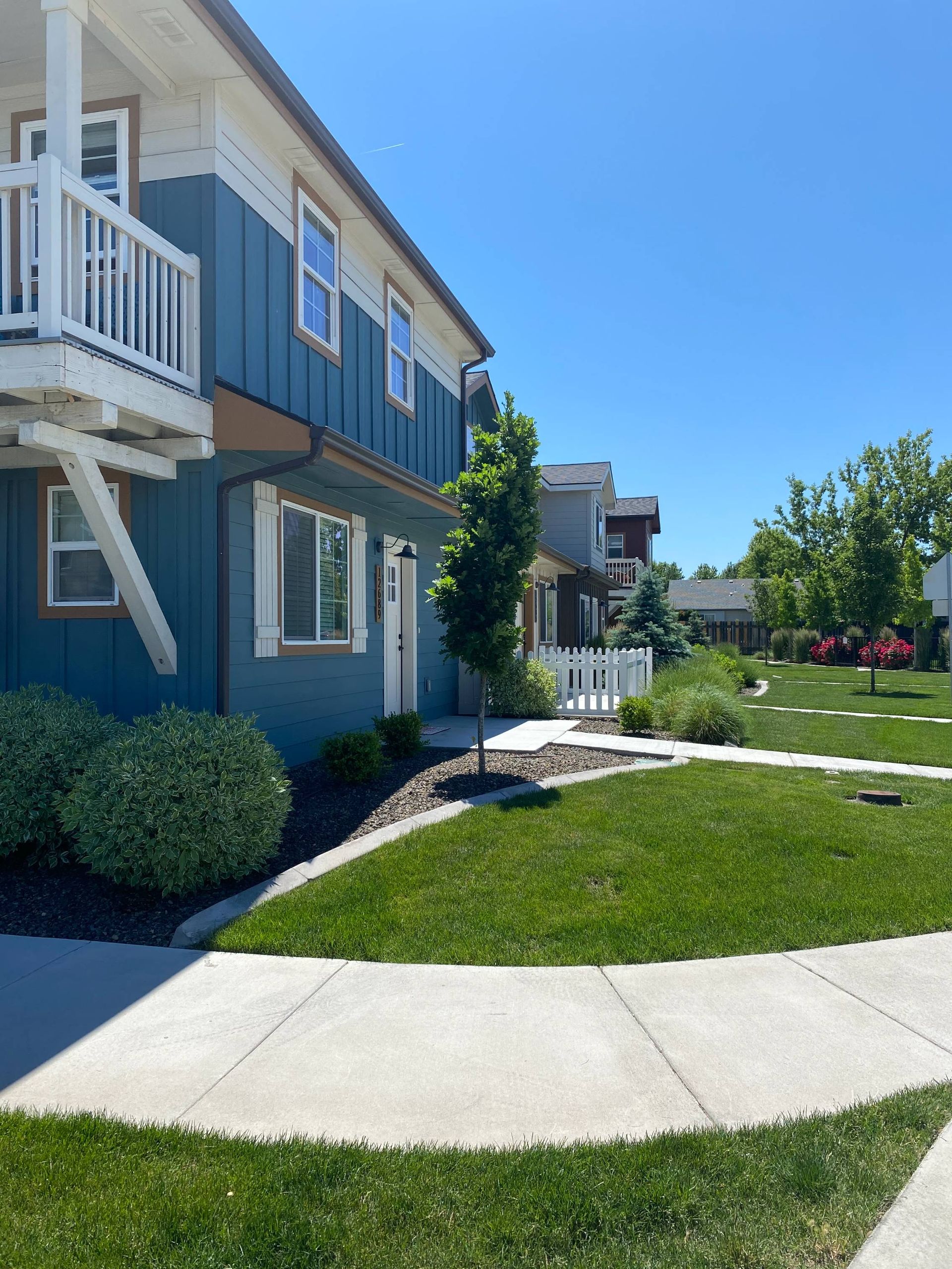 Blue and white townhouse with a green lawn and sidewalk. Sunny day.