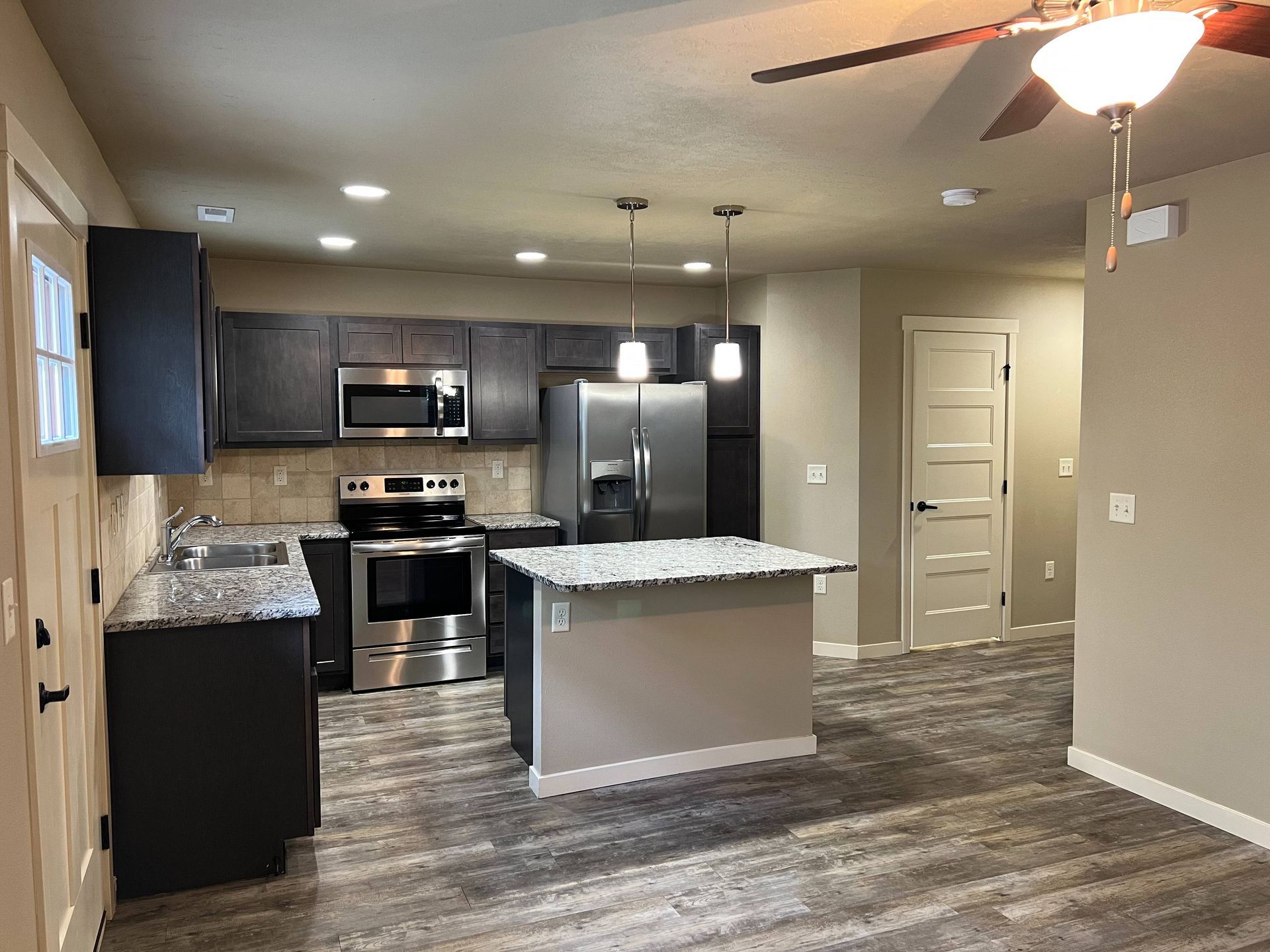 Kitchen with dark cabinets, stainless steel appliances, and island with granite countertop.