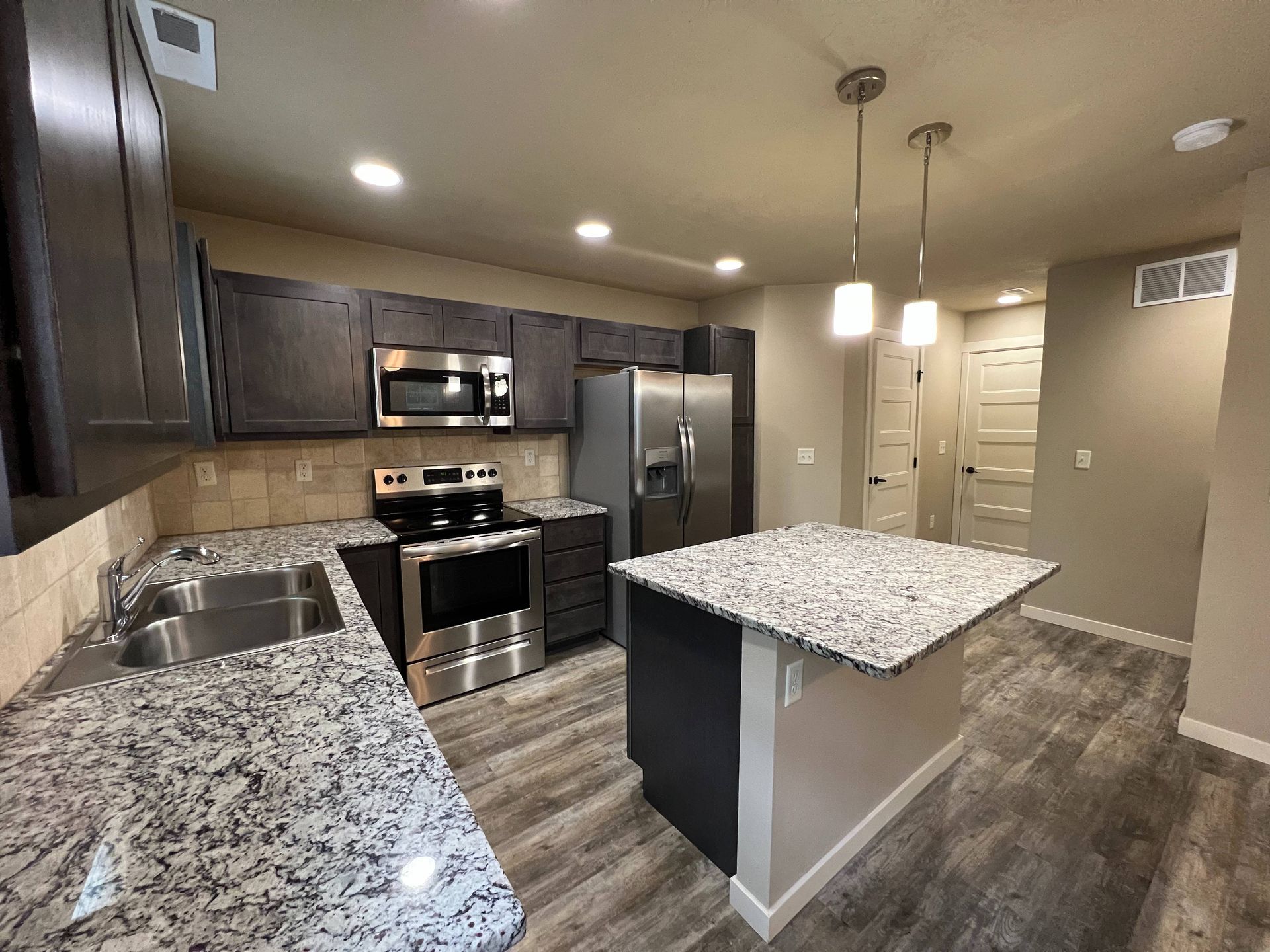 Modern kitchen with granite countertops, stainless steel appliances, and dark cabinets.
