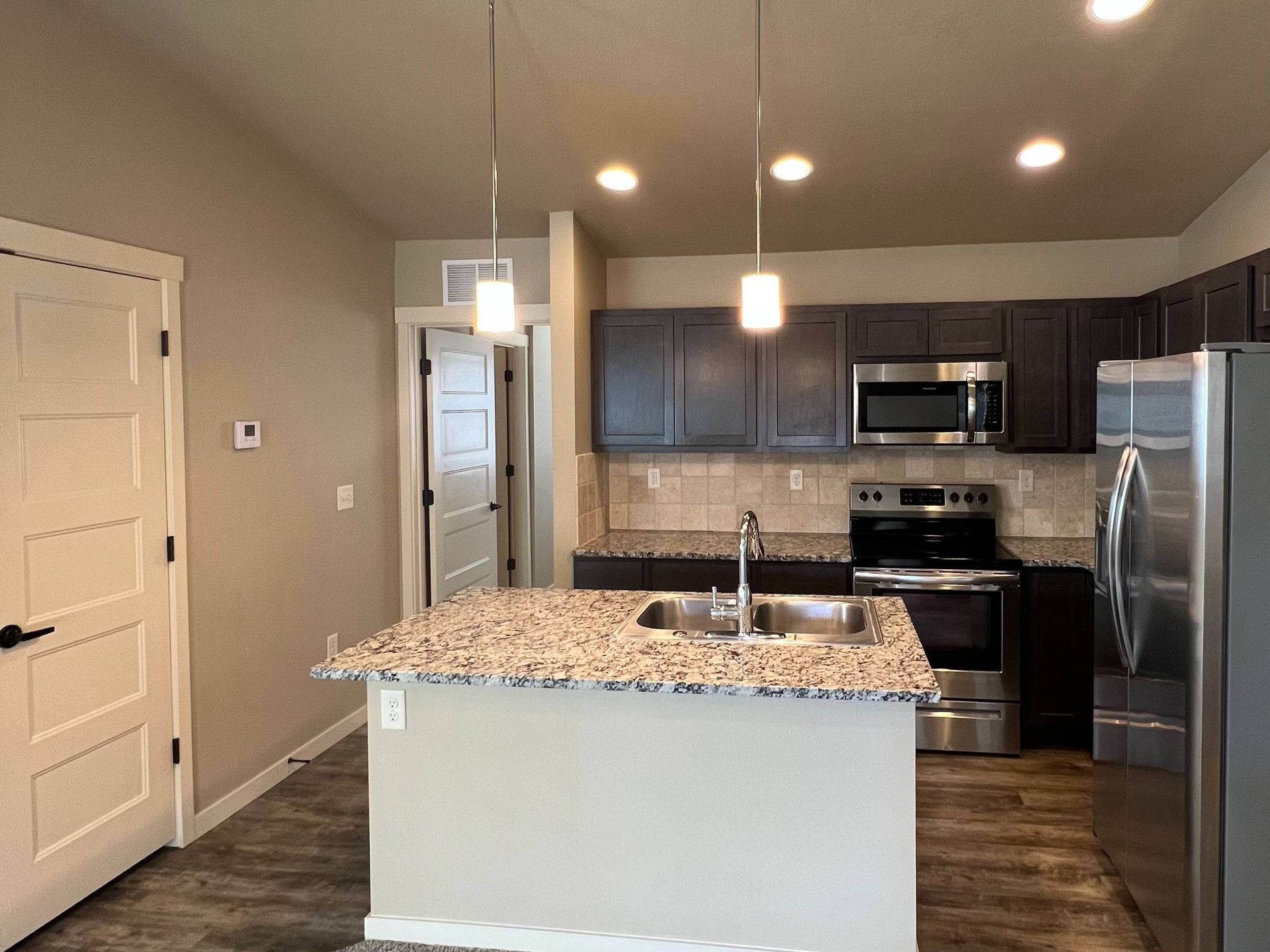 Kitchen with island, dark cabinets, granite counters, stainless steel appliances, and wood floor.