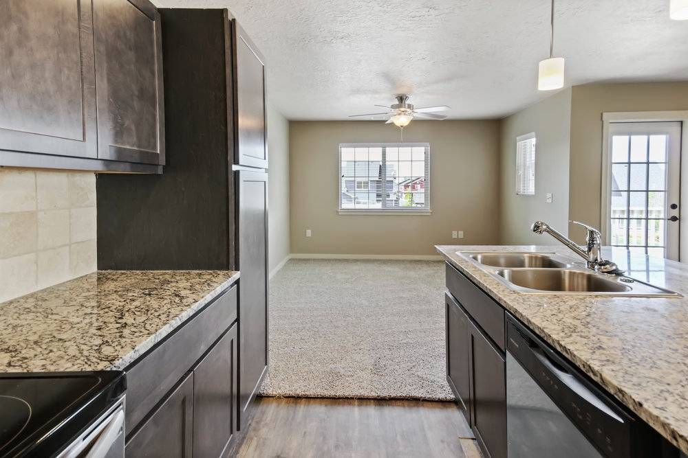 Kitchen with granite countertops, stainless steel sink, and a view into a living room with a window and a door to a balcony.