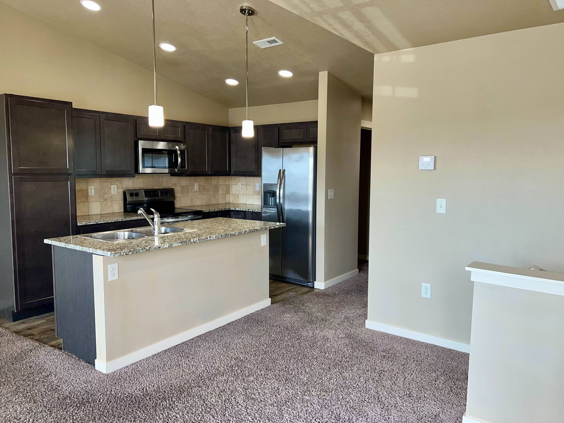 Modern kitchen with dark cabinets, stainless steel appliances, and a granite countertop island.