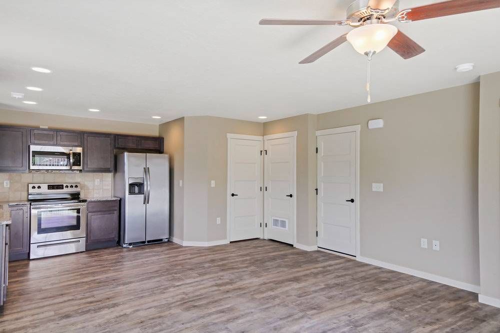 Open-concept living space with kitchen and living area, brown cabinets, stainless steel appliances, and wood-look flooring.