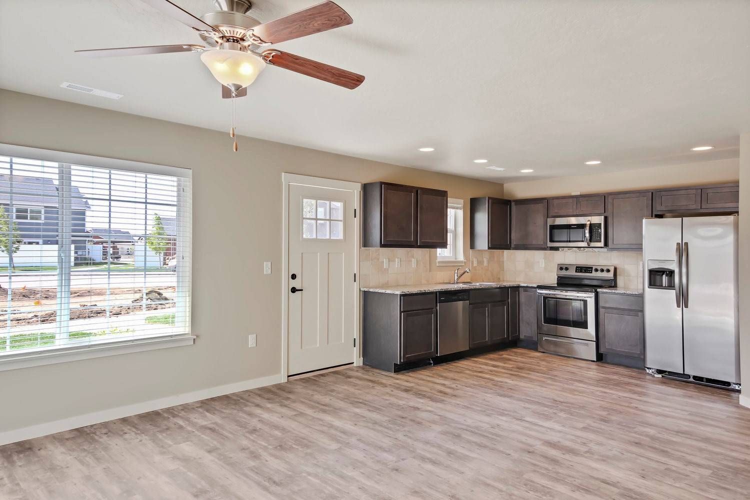 Open-concept kitchen and living area, featuring gray cabinets, stainless steel appliances, and wood-look flooring.