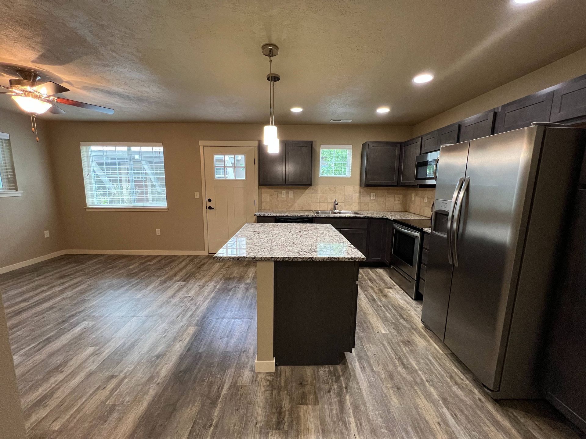 Modern kitchen with island, stainless steel appliances, dark cabinets, and wood-look flooring.