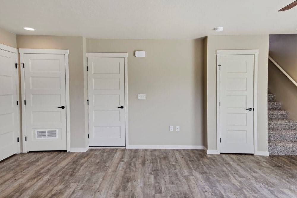 Interior view of a room with three white doors, wooden floor, and a staircase on the right.