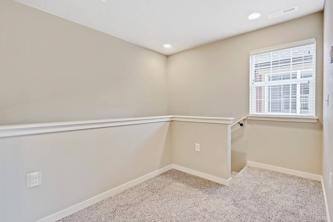 Empty room with beige walls, white trim, small window, and light-colored carpet.