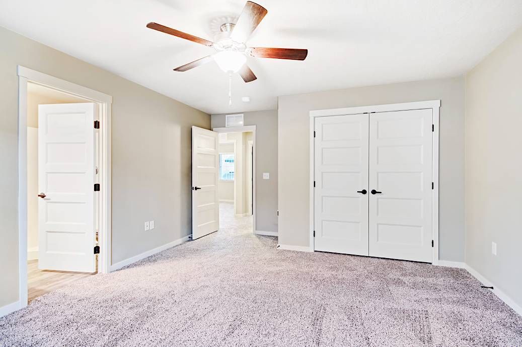 Empty bedroom with a plush carpet, white doors, and a ceiling fan.