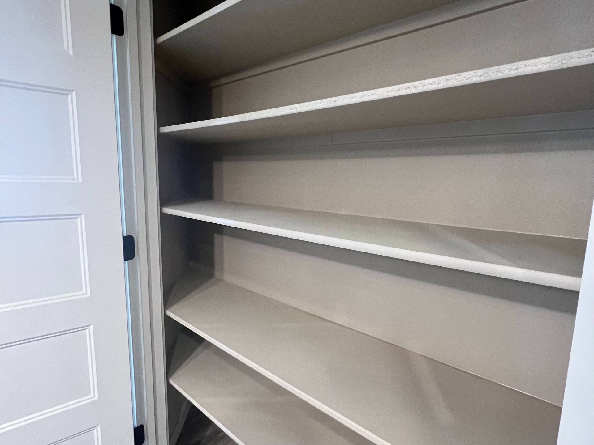 Empty white shelving unit inside a white closet, doors partially visible.