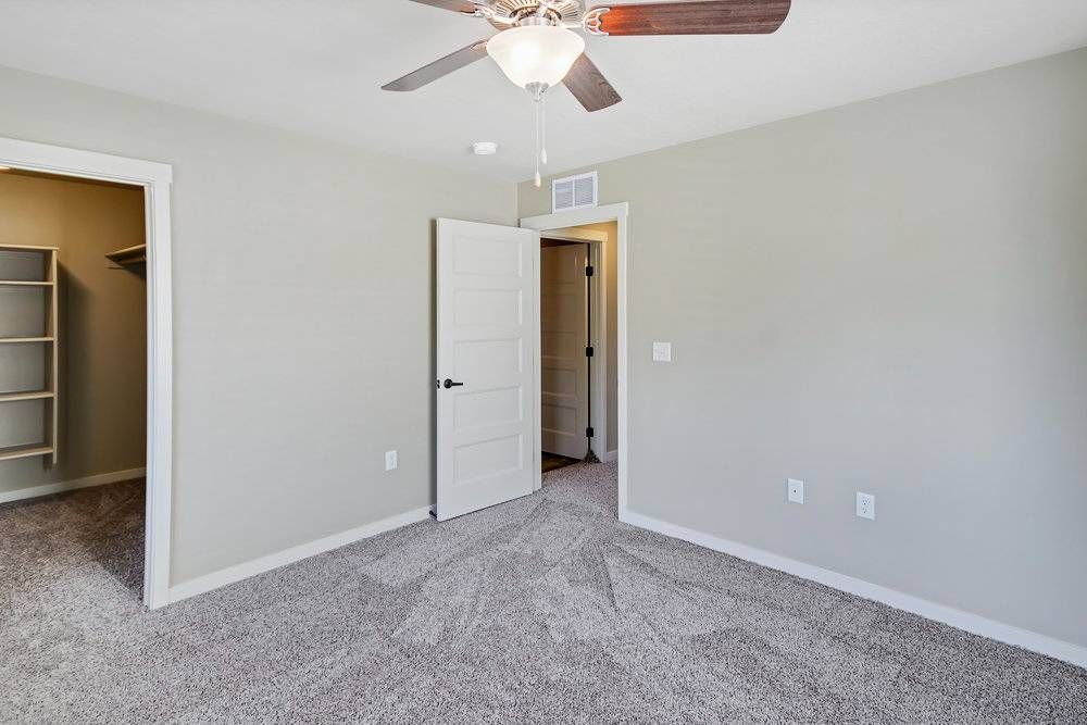 Empty bedroom with gray carpet, walls, and ceiling fan. White door and closet.