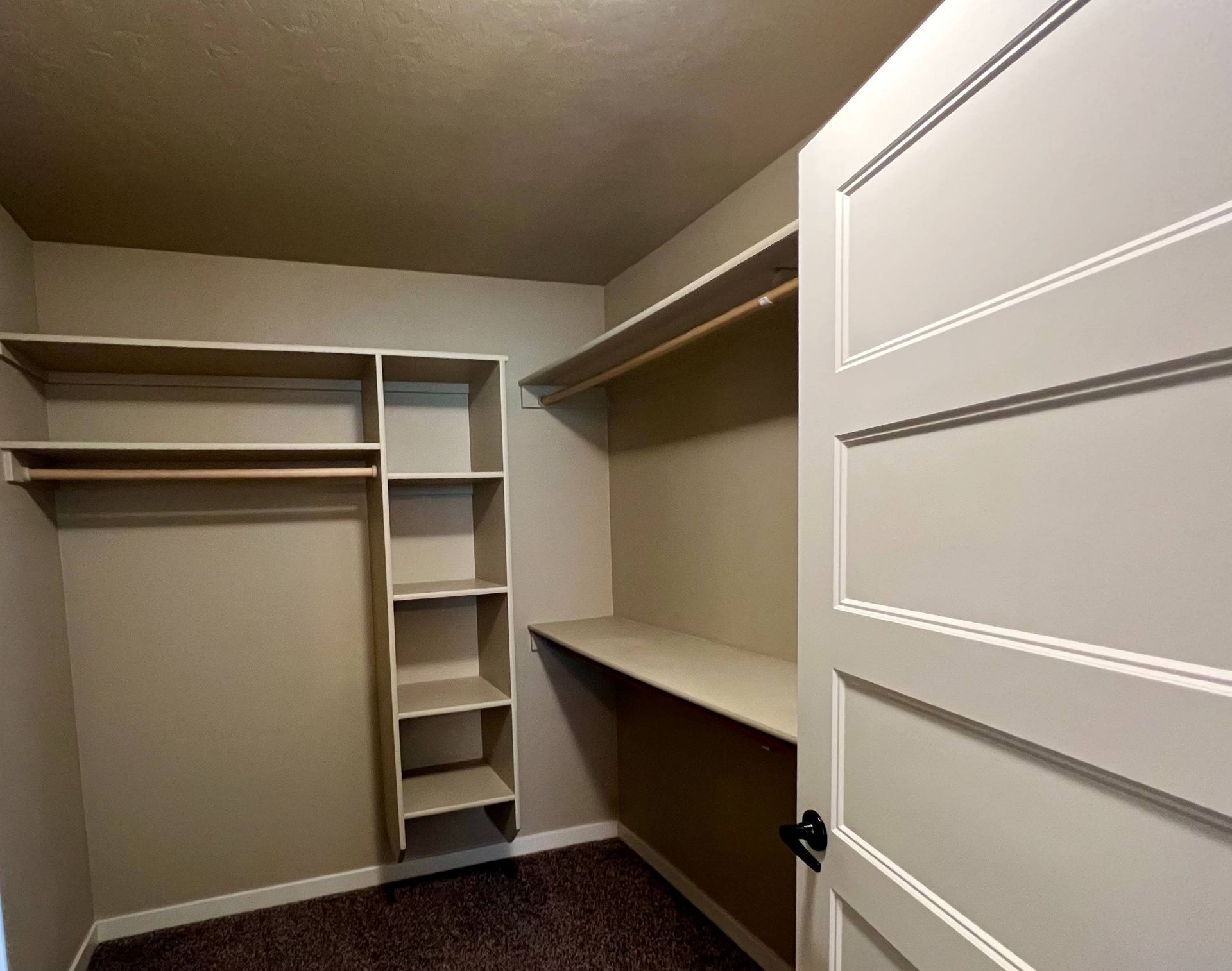 Empty closet with shelves, a clothes rod, and a built-in desk. Beige walls and white door.