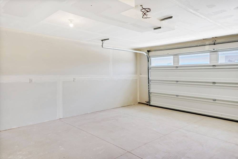 Empty, unfinished garage interior with white walls, ceiling, and concrete floor; garage door open.