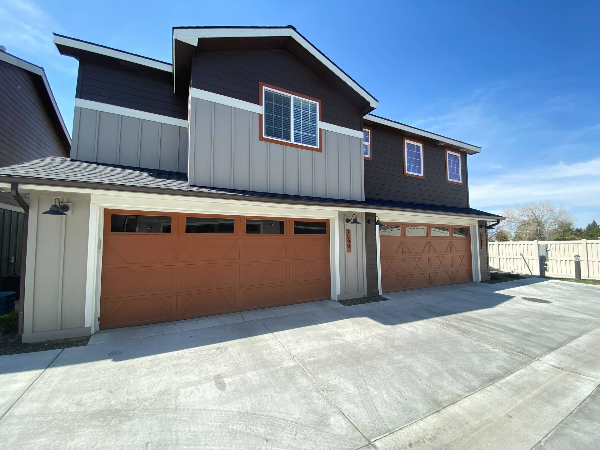 Two-story brown and gray house with a small front porch, beside a sidewalk and gravel landscaping.