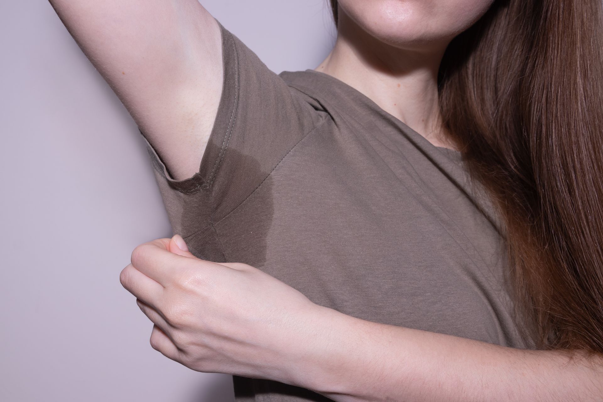 Person lifting arm to show underarm hair, wearing a gray shirt against a plain background