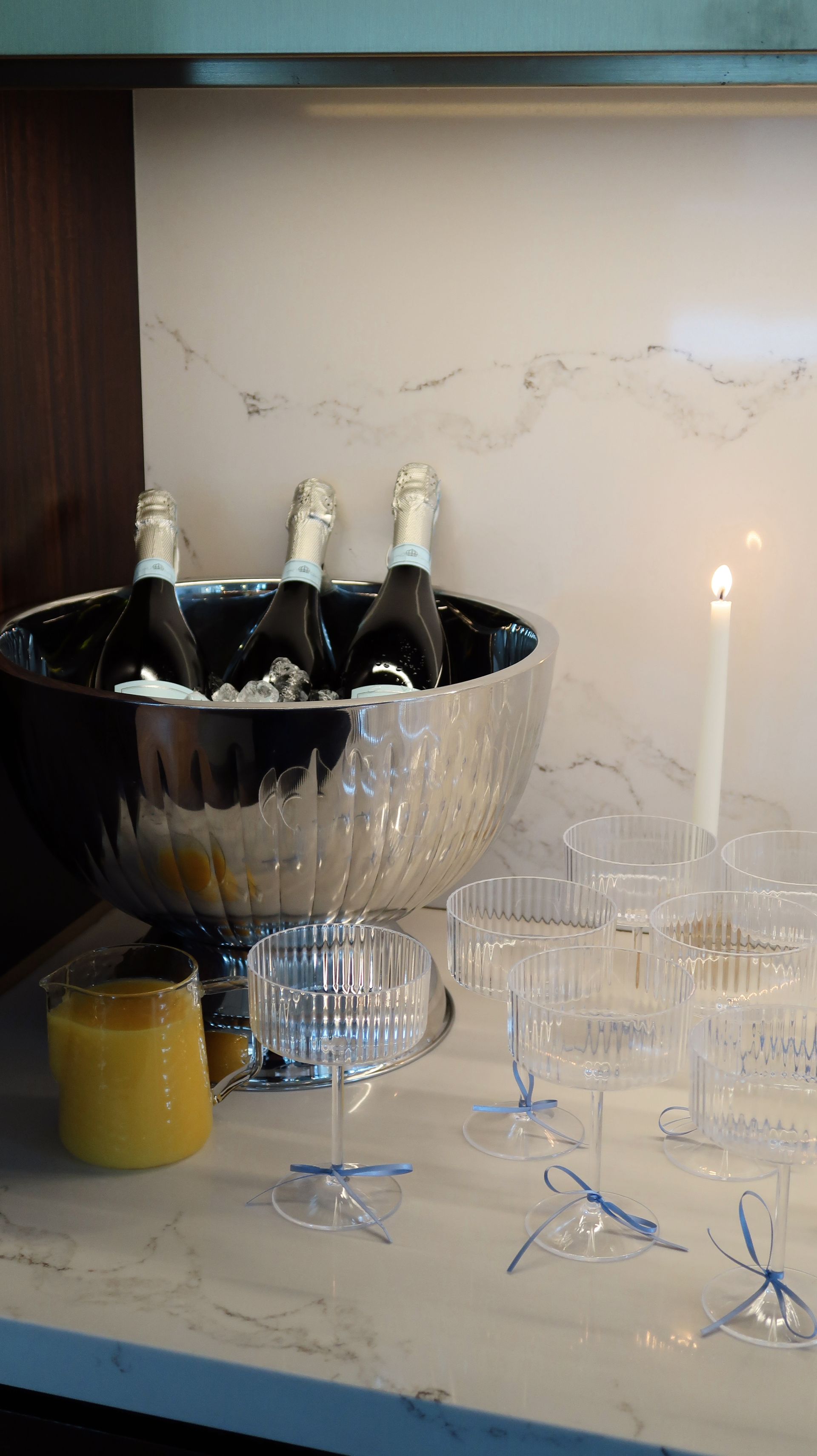 Champagne bottles in an ice bucket beside glassware and a lit candle on a table