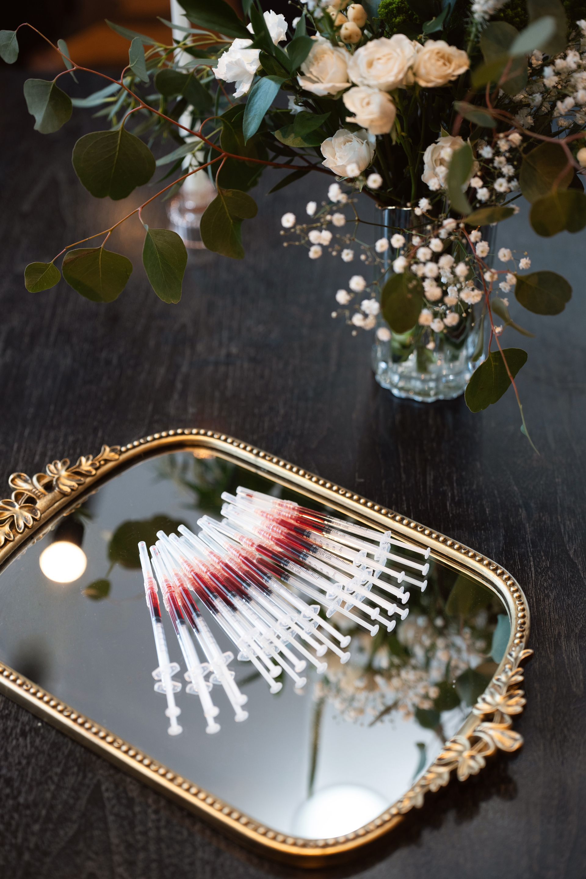 Decorative mirror tray on dark table with a floral arrangement and white-red swatches reflected in the glass