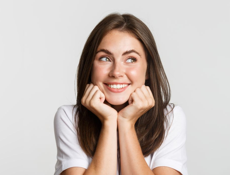 Smiling woman in a white shirt resting her chin on her hands and looking upward