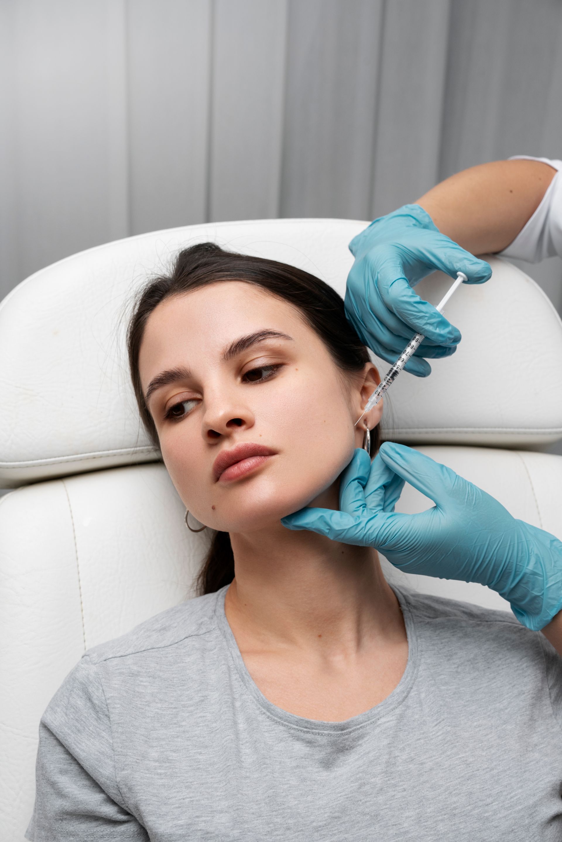 Medical professional adjusting earrings on a seated patient in a treatment chair