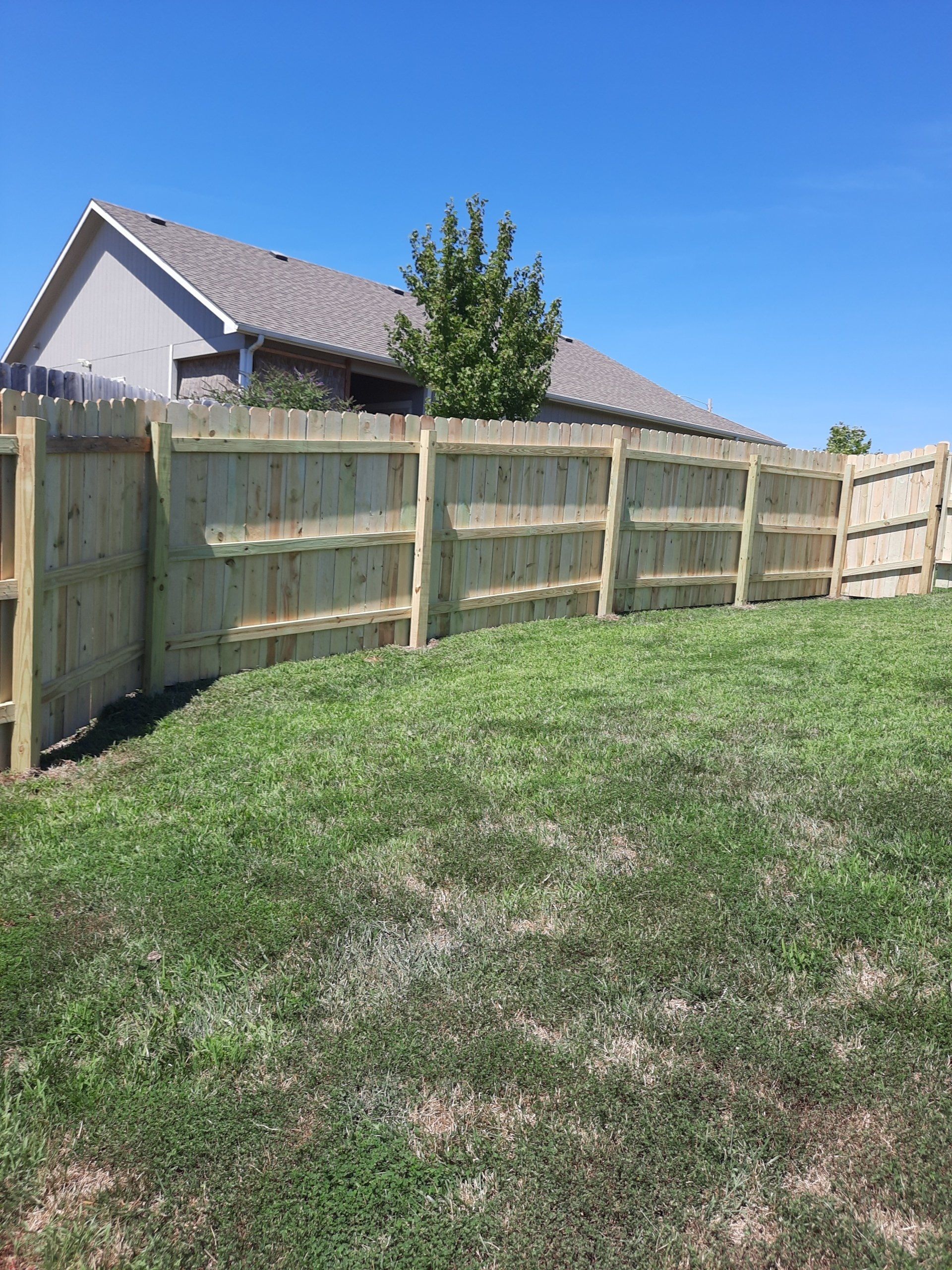 A wooden fence surrounds a lush green field in front of a house.