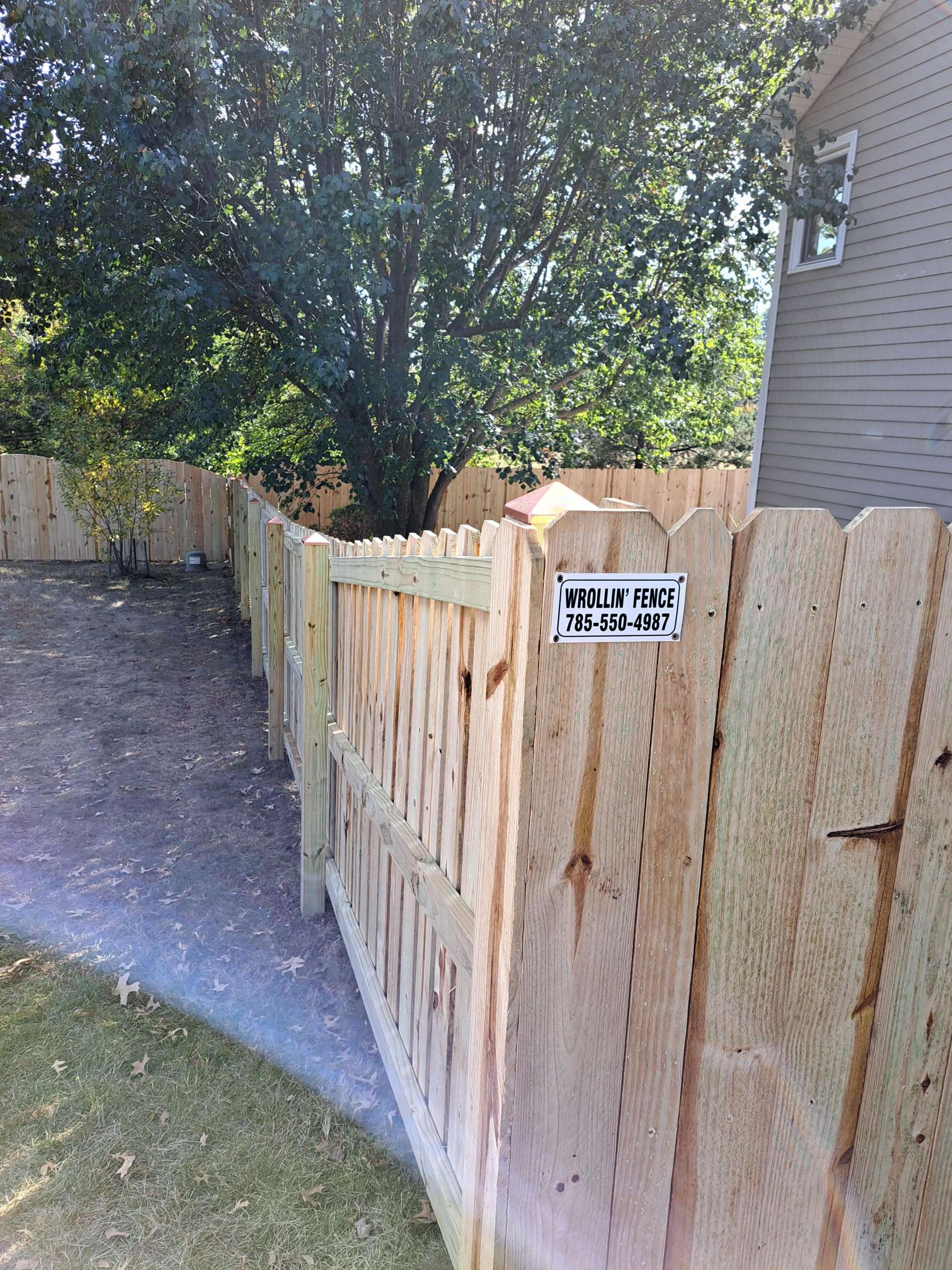 A wooden fence with a sign on it is next to a house.