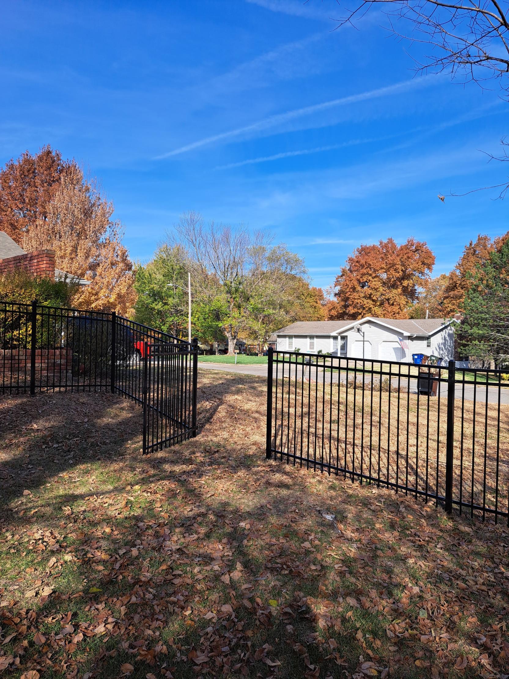 There is a fence in the middle of a field with a house in the background.
