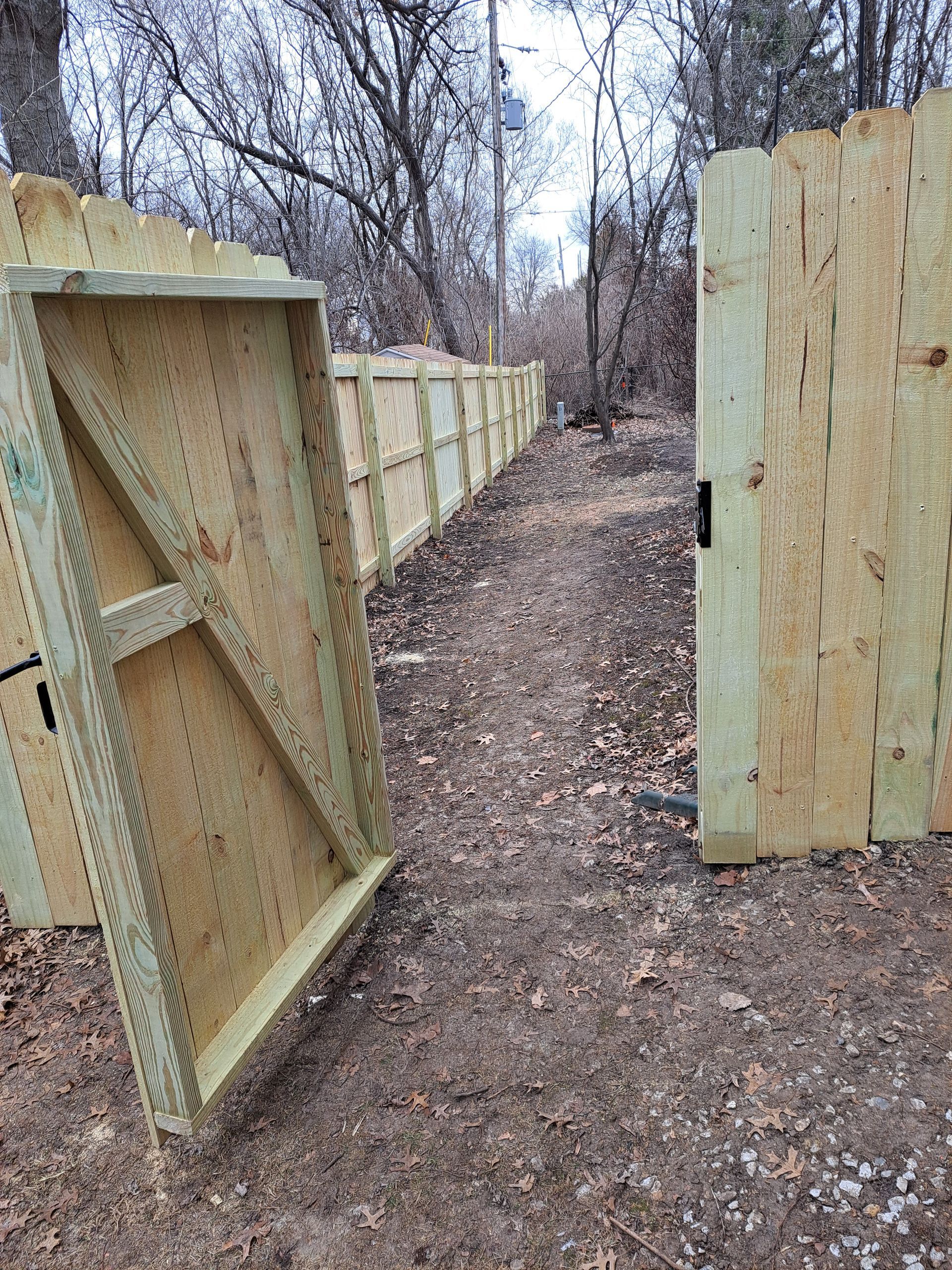 A wooden fence is sitting on top of a dirt path next to a wooden gate.