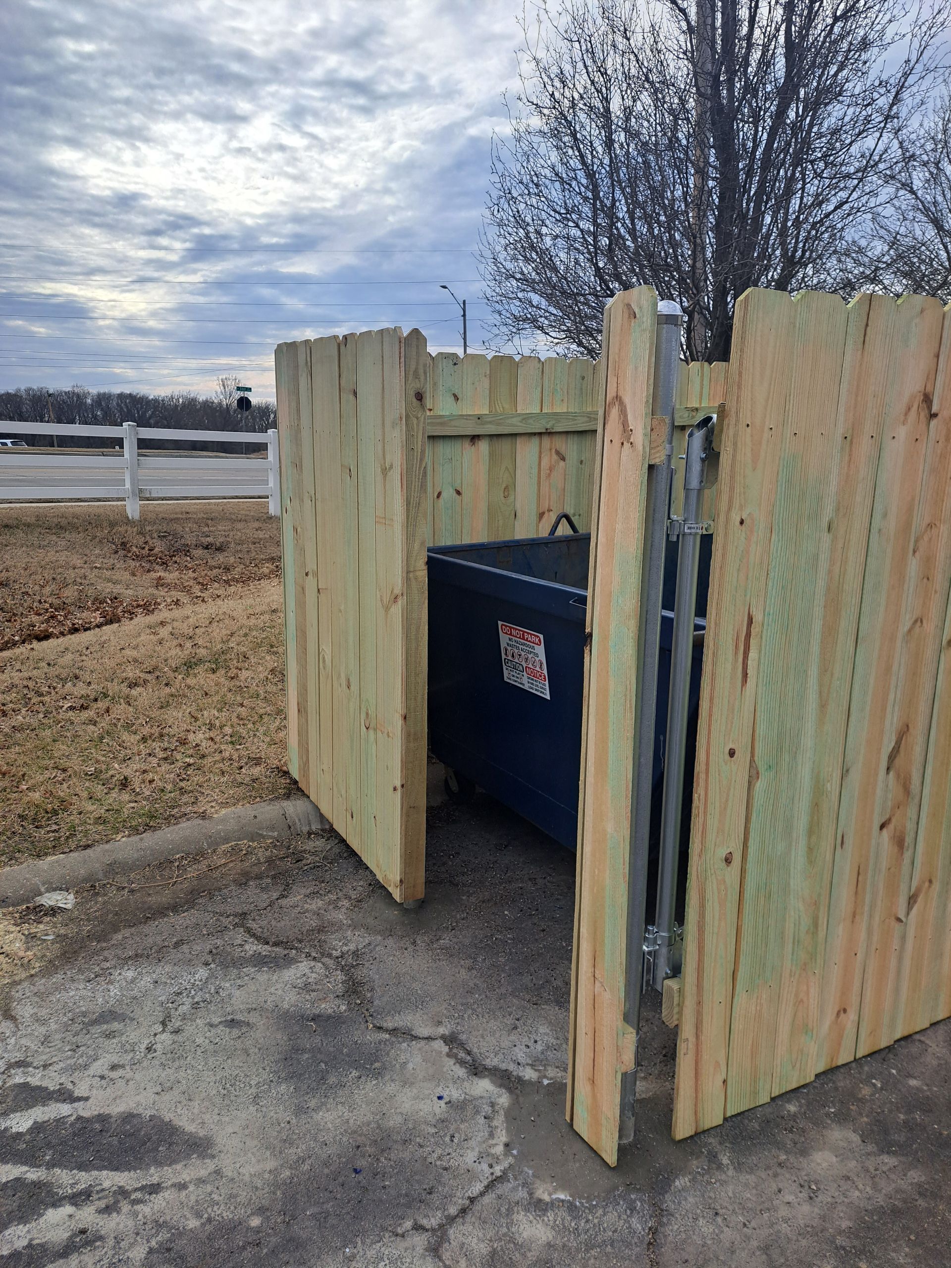 A wooden trash can is behind a wooden fence.