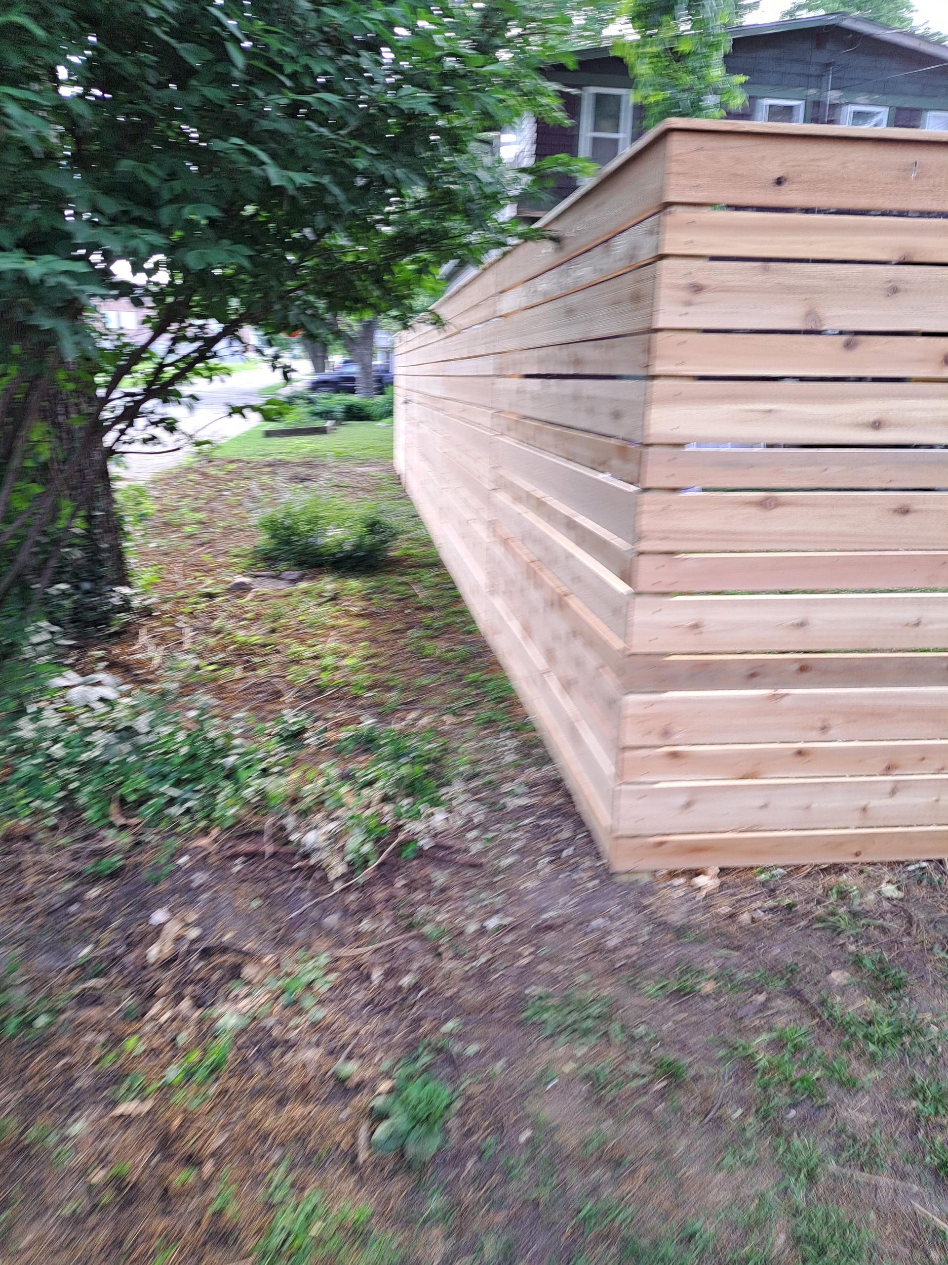 A wooden fence is sitting in the middle of a yard next to a tree.