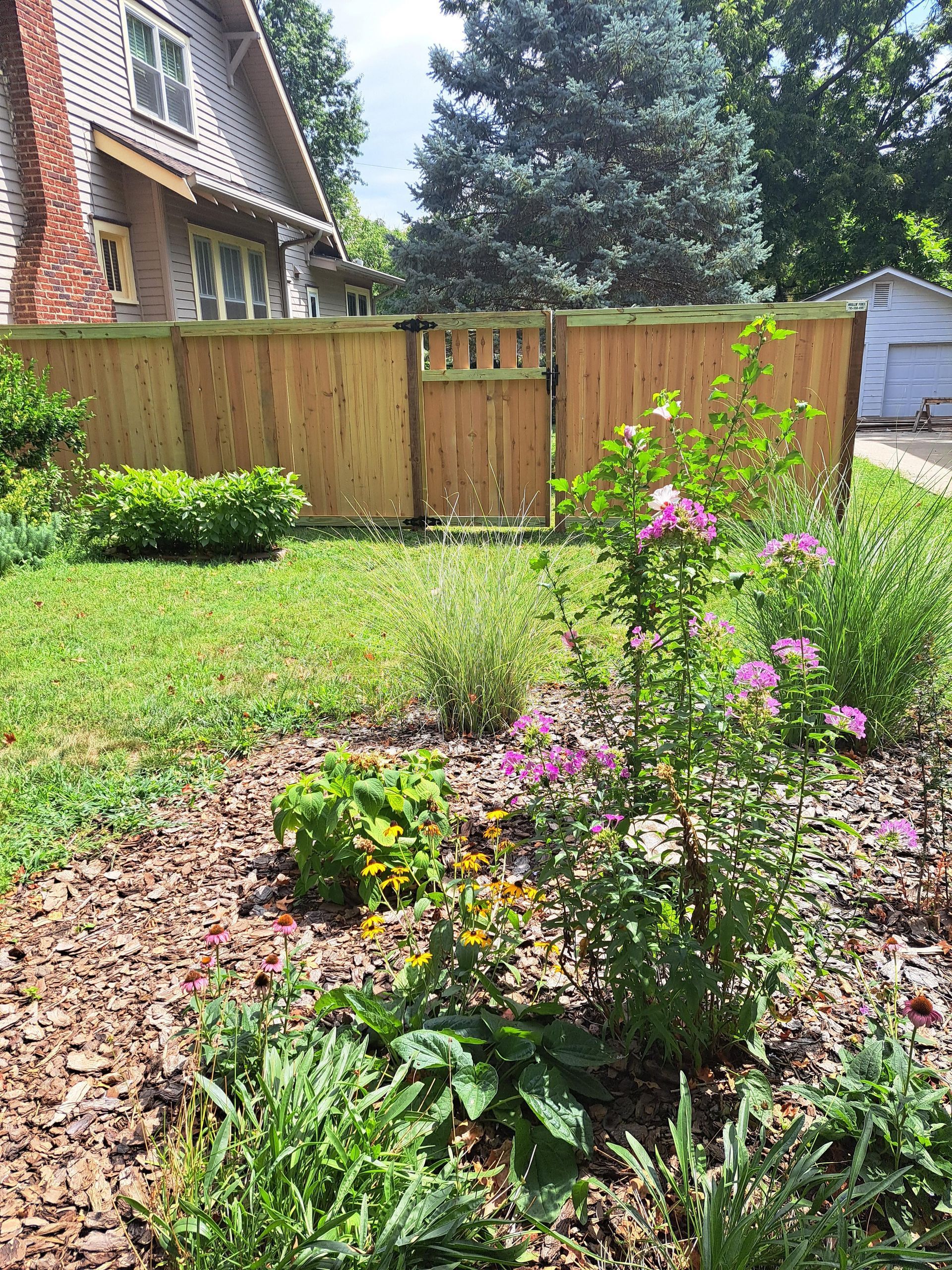 A garden with flowers and a wooden fence in front of a house.