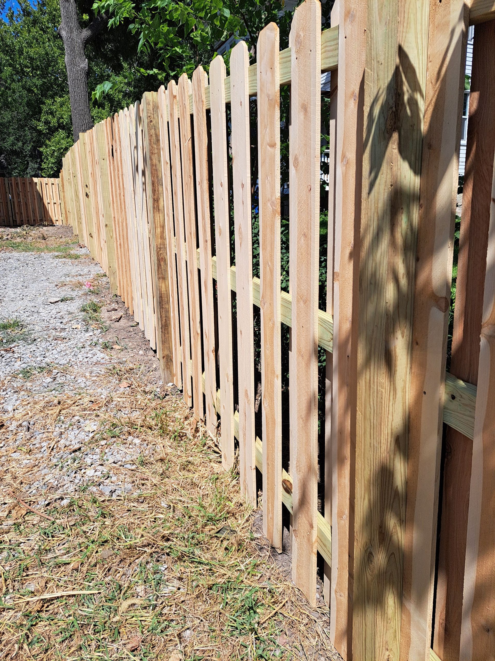 A wooden picket fence is sitting next to a dirt road.