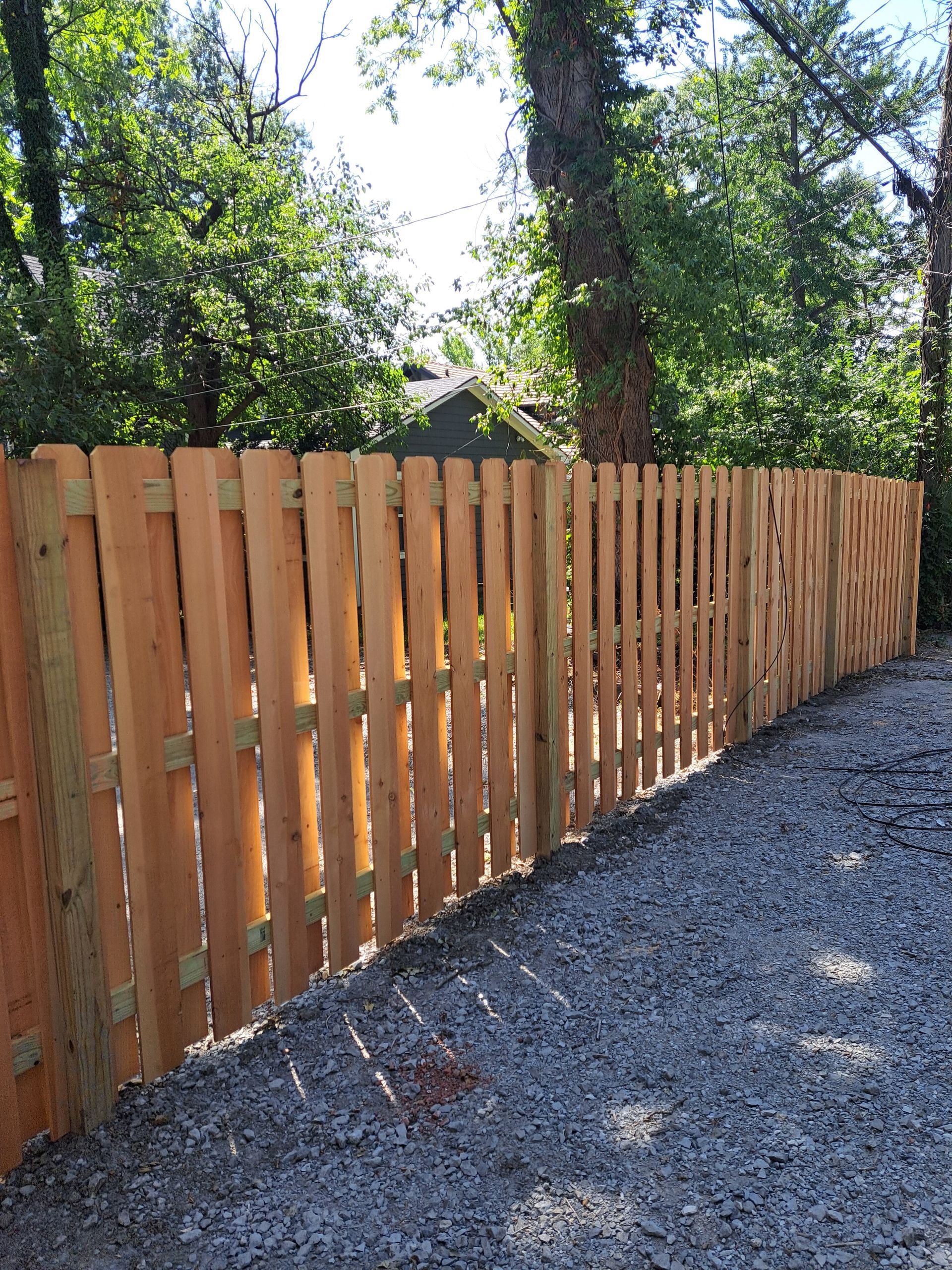 A wooden fence is surrounded by gravel and trees.