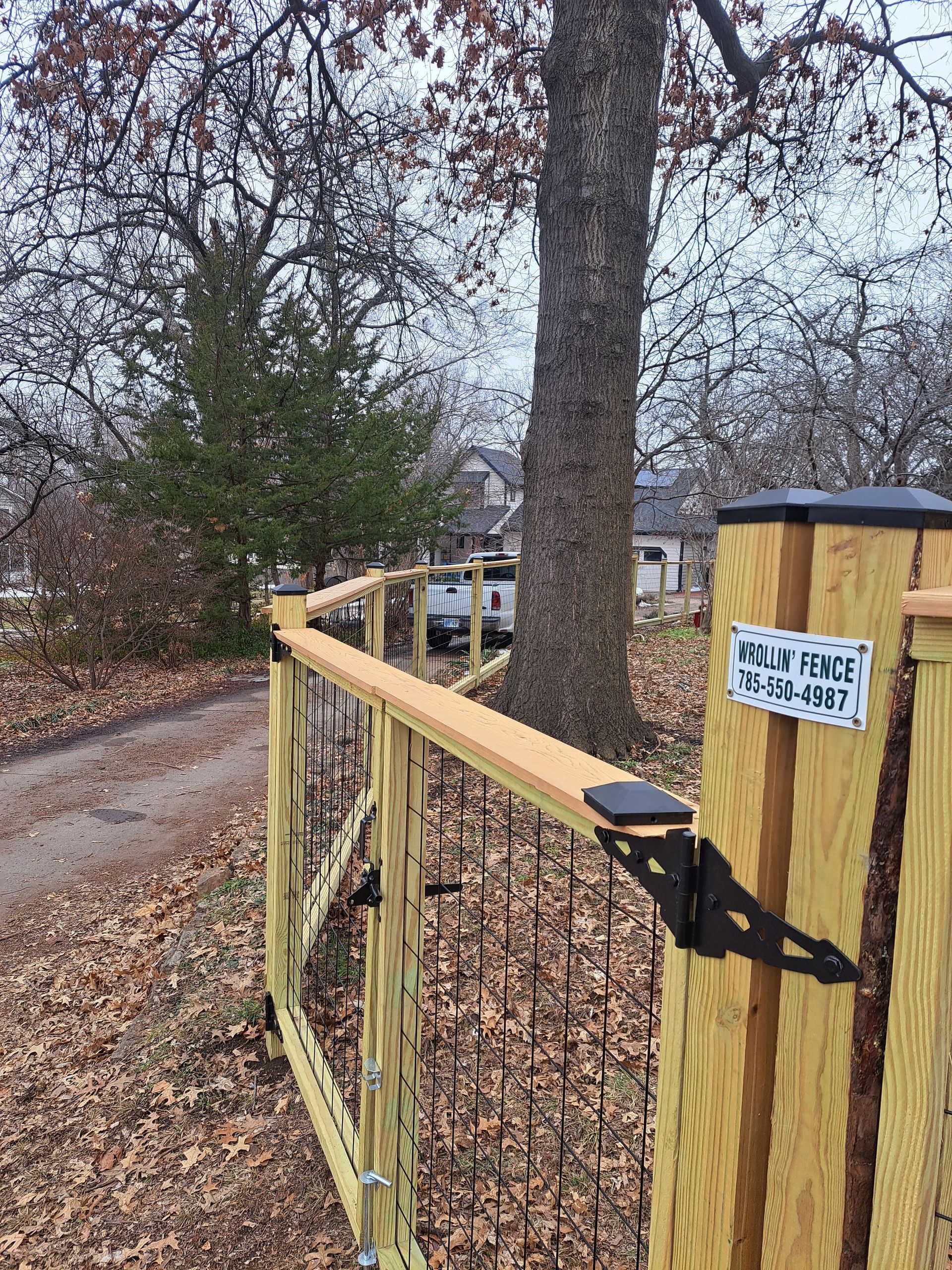 Wooden fence with black metal accents; gravel driveway leads to a house.