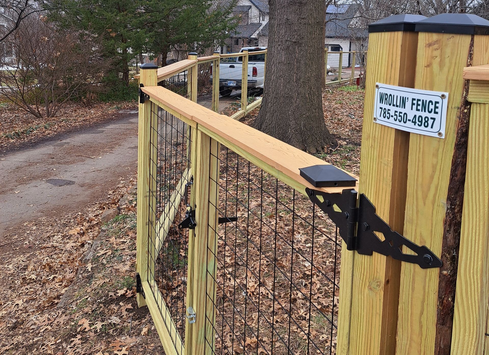 A wooden fence with a black trash can in front of it