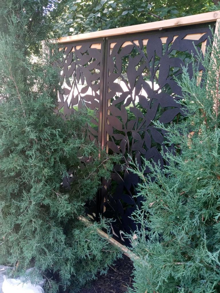 A black fence with leaves on it is surrounded by trees.