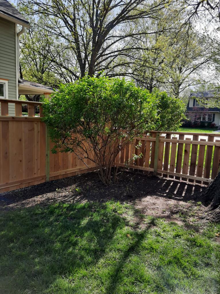 A wooden fence surrounds a lush green yard in front of a house.