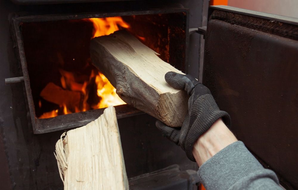 Person Wearing Black Glove Placing a Log Into a Wood-burning Stove — Climate King In Cowra, NSW