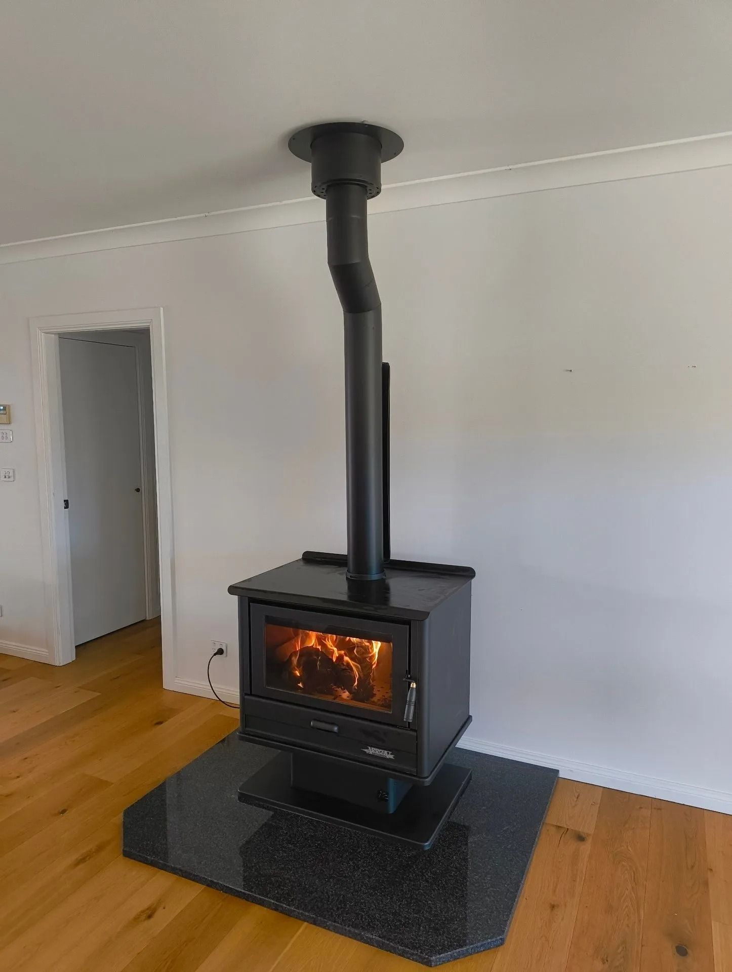 Black Wood-burning Stove With Lit Fire, Chimney, on a Granite Base — Climate King In Orange, NSW