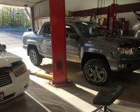 A truck is sitting on a lift in a garage next to a car.