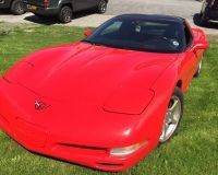 A red corvette is parked in the grass in a driveway.