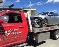 A red tow truck is towing a damaged car.