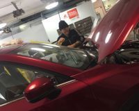 A man is working on a red car in a garage with the hood open.