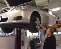 A man is standing next to a car on a lift in a garage.