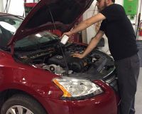 A man is looking under the hood of a red car.