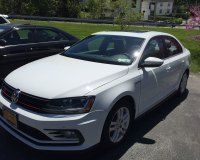 A white volkswagen jetta is parked in a driveway next to a black car.